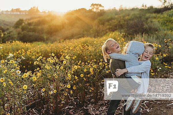 Siblings hugging at sunset in field of flowers