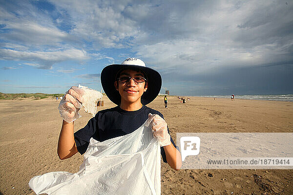 A young boy poses for the camera while cleaning up the beach.