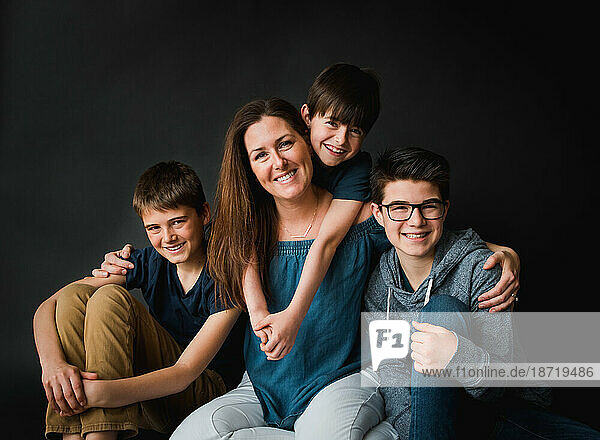 Portrait of a mother and her three sons against a black background.