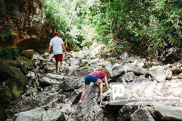 Young girl climbing rocks while hiking with dad