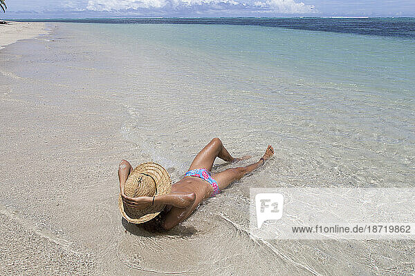 Man wearing straw hat and blue speedo  tanning on idyllic sandy beach