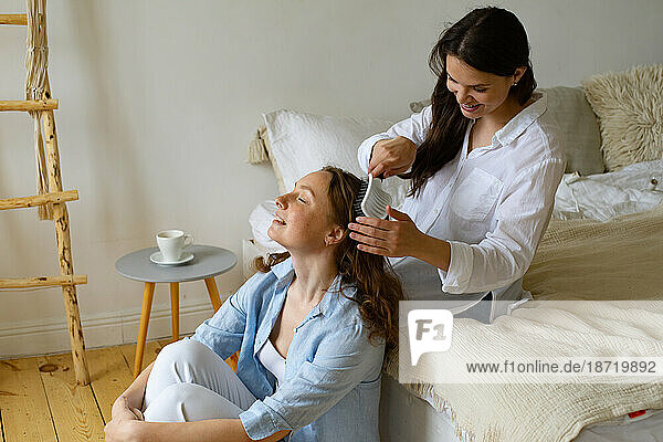 Two young women sitting together at home  one brushing another's hair