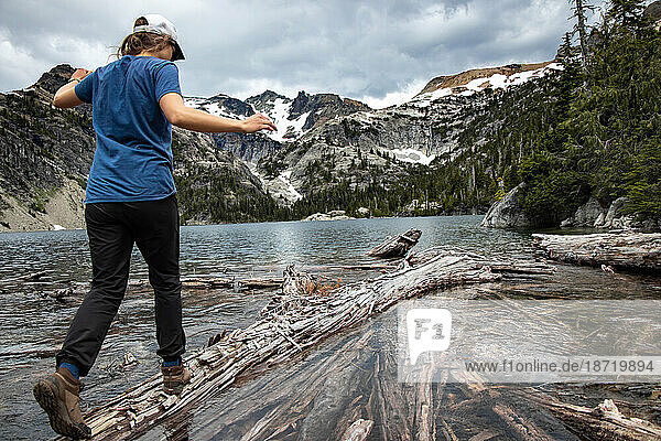 Young hiker girl balances across narrow log on wild mountain lake