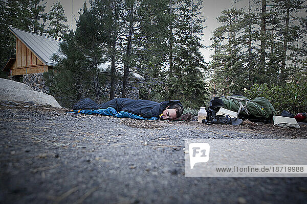 A hiker sleeps in a parking lot .