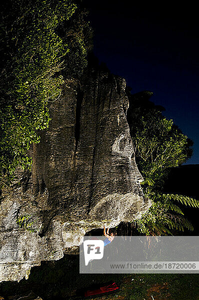 Illuminated at dusk  a young woman rock climbs an overhanging fin of limestone  Waitomo  New Zealand.
