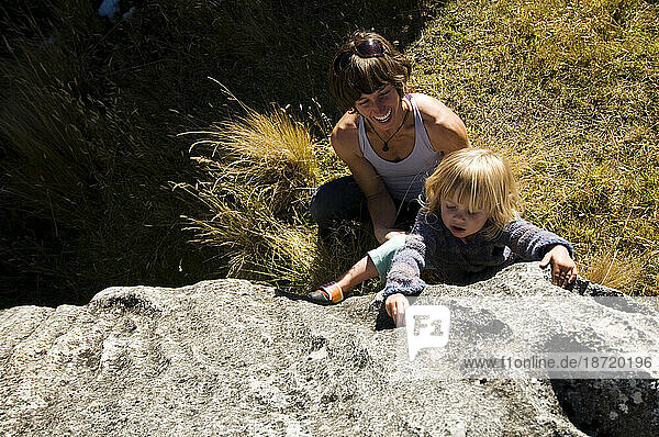 A mother encourages her young daughter to climb a limestone boulder in Castle Hill  New Zealand.