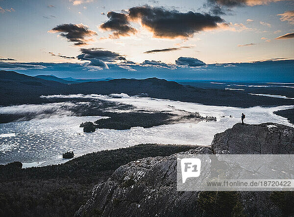 lone hiker stands on rocky summit with lakes and mountains  sunrise