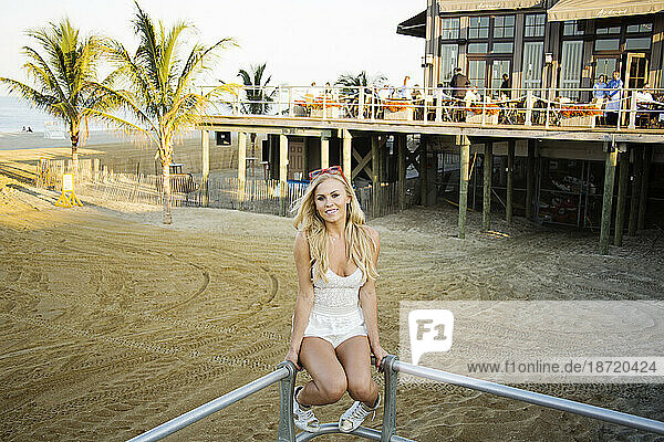 Blonde woman sitting on stair railing overlooking beach