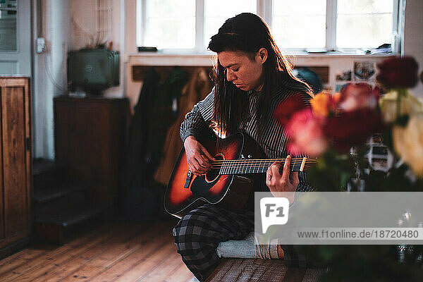 Asian person relaxes at home playing guitar in wooden house sun