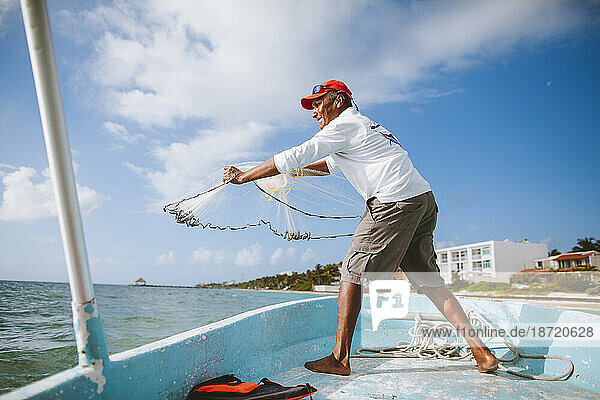 A deep sea fisher casts a net off the side of a boat near shore