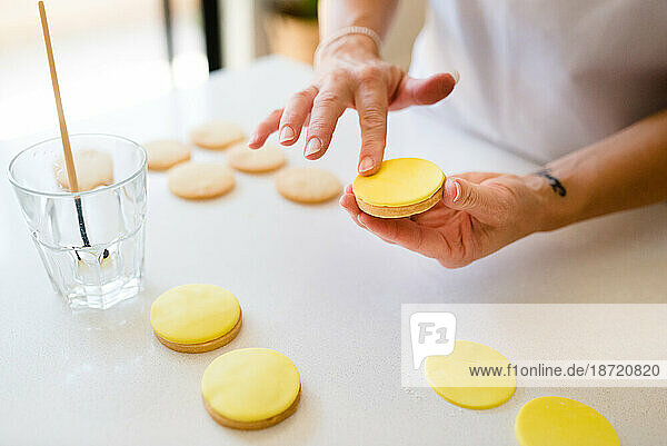 A woman's hands decorating cookies with yellow fondant