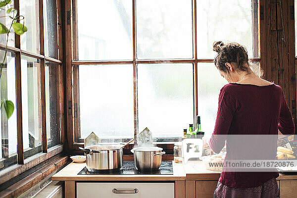 young woman cooks at home in natural wooden kitchen with large window