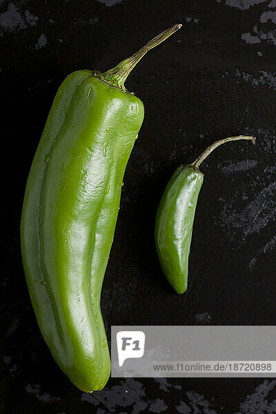 Two types of organic hot green peppers sit on a wet black cutting board in a home kitchen in Seattle  Washington.
