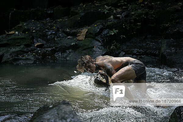 Young tattooed man swims in a mountain river in Bali.
