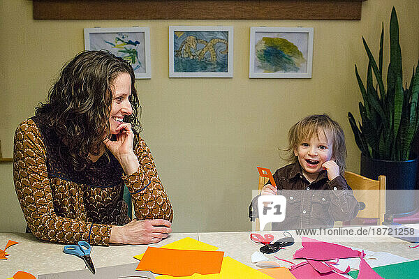 A smiling mom and small son create art together at dining room table
