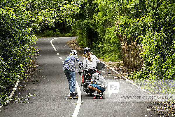 Two longboarders carrying behind motorbike carrying third skateboarder