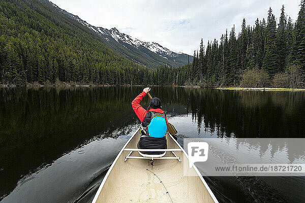 Rear view of woman canoeing on Kingdom Lake with trees and mountains.