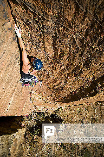 5.11 sandstone route with female climber. Crack climbing  taped hands  helmet. Steep vertical route.