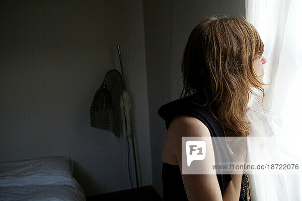 A young woman looking out of the window of her bedroom  Los Angeles  California.