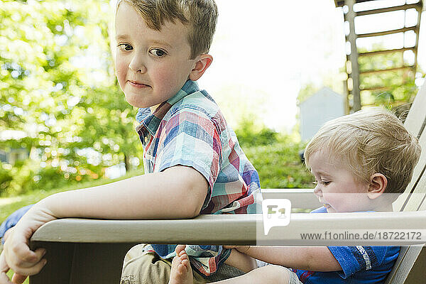 Younger brother tries to push older brother out of chair in backyard