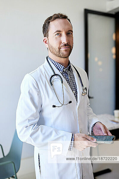 Portrait of male doctor holding smart phone while standing in clinic