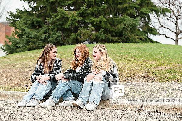 Three happy teen girls sitting on a curb.