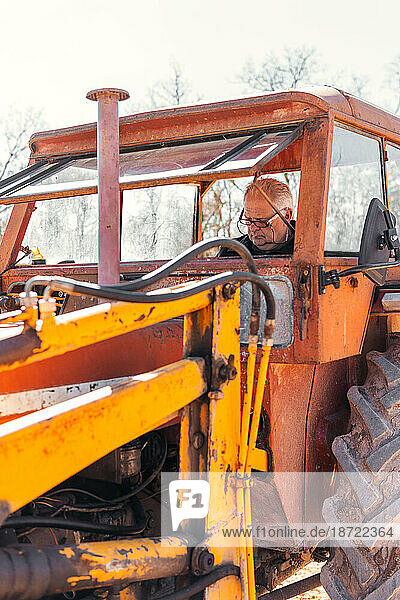 modern gray-haired gentleman with glasses riding a tractor