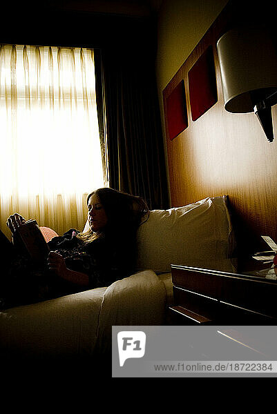 A woman reads a book while laying in bed at a hotel in San Francisco  California.