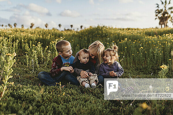 Four siblings smiling at each other in field of flowers with blue sky