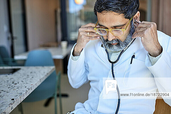 Mature male doctor adjusting stethoscope in clinic
