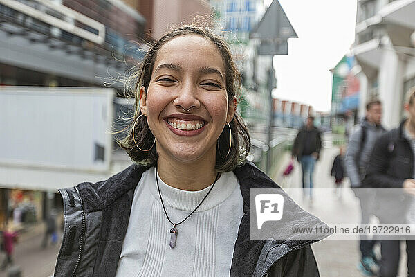 Smiling young mixed race woman with piercing nose and ears on street.