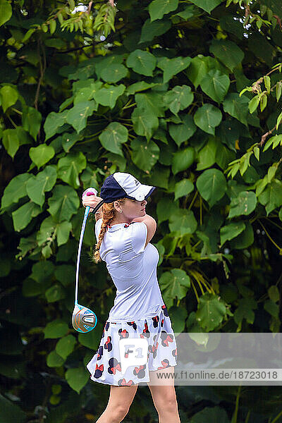 Side view of young woman in hat playing golf