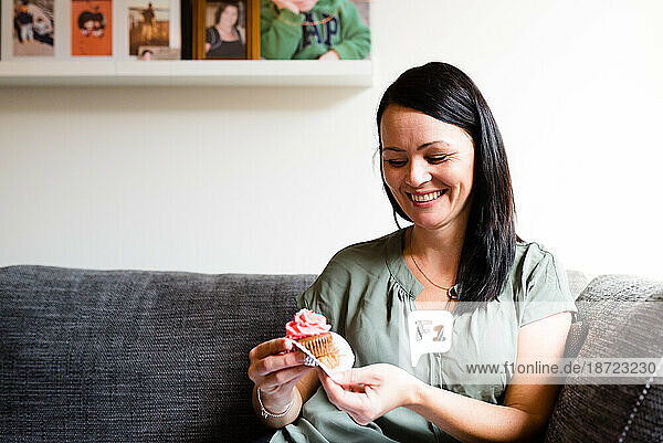 A female smiling while having a cupcake on a sofa at home