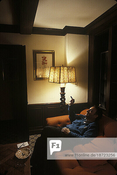 The former chairman of a large financial company relaxes with a cigar in the dimly lit living room of his Connecticut home.