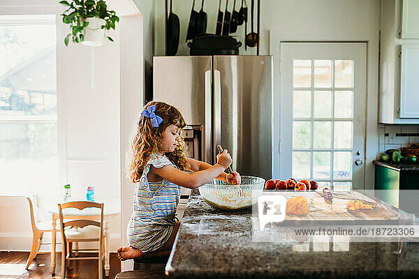 Young girl sitting in kitching mixing peach muffin batter