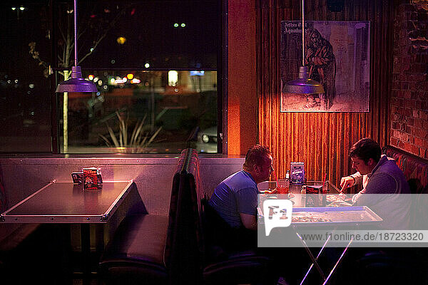 Two men sit at a table eating pizza at a dimly lit restaurant in Federal Way  Washington.