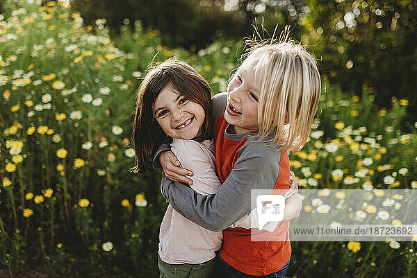 School-aged boy and girl hugging in field of flowers