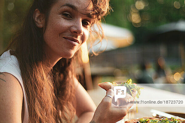 woman smiles as she eats organic pizza in golden sun outside cafe