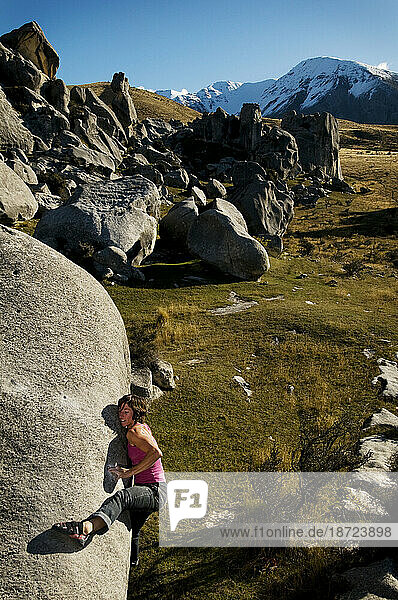 A young woman rock climber struggles up the smooth lip of a limestone boulder in Castle Hill  New Zealand.