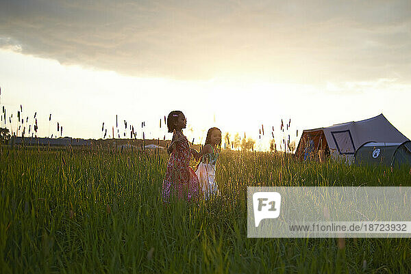 Two young girls happily running hand in hand in a field of high grass