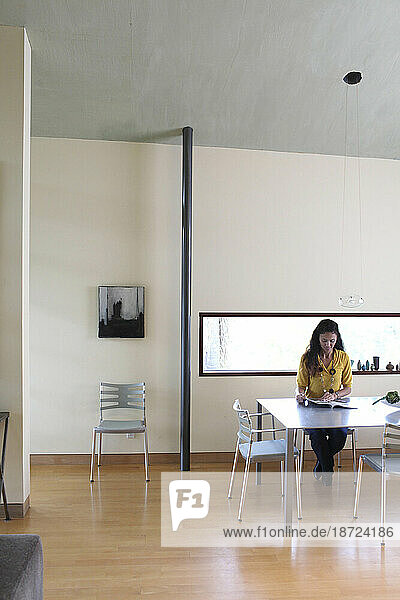 An Asian American woman sits in a chair inside a modern home and reads a magazine on a table in Del Mar  California.