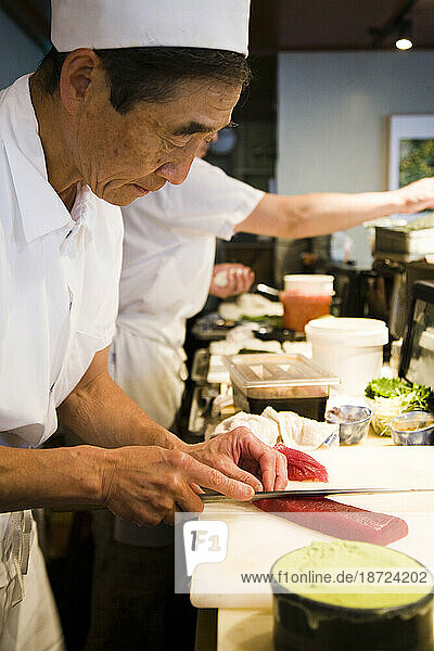 A sushi chef slices fresh  raw fish at his restaurant.