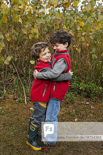 two smiling little boys embrace in a hug outdoors