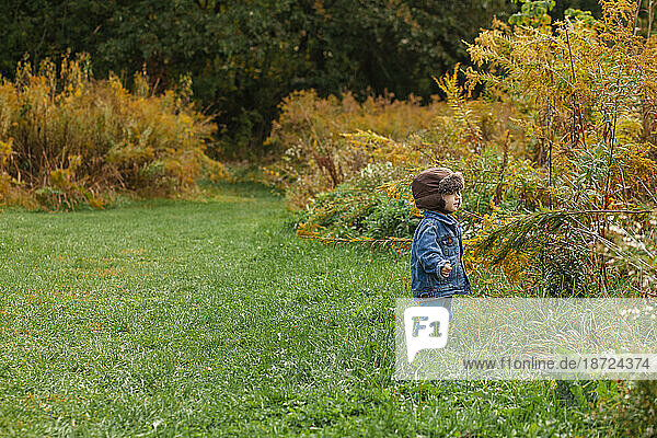A small toddler stands bundled up in a golden field in autumn