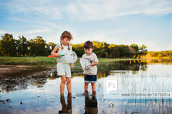 Young girl and boy looking at fish in their fishing nets at the lake