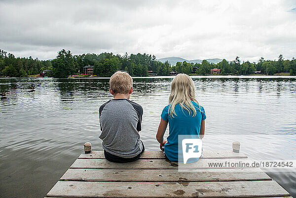 Girl and boy sitting at the edge of dock of lake