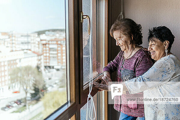two elderly female friends looking out the window of their house