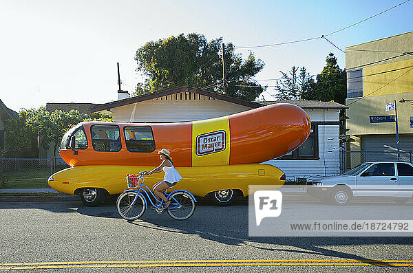 A woman rides past a parked Oscar Mayer Weinermobile in Venice  Los Angeles  California.
