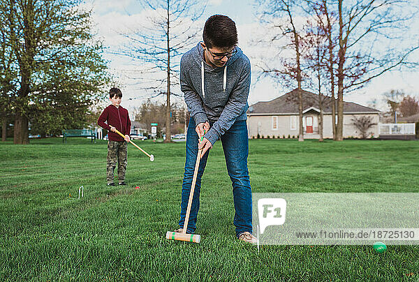 Two boys playing a game of croquet in a park together.