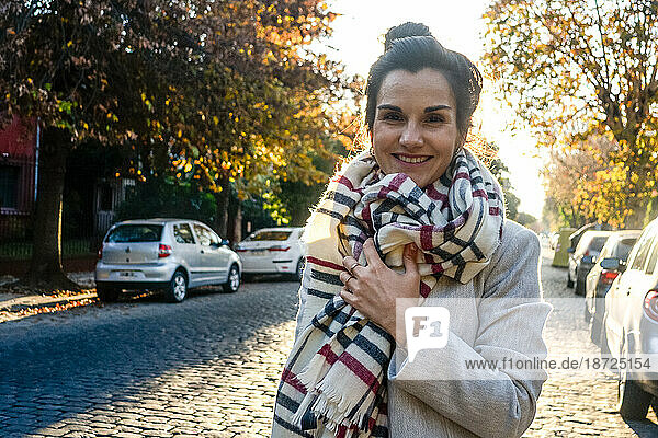 Portrait of smiling young woman with scarf standing on the street